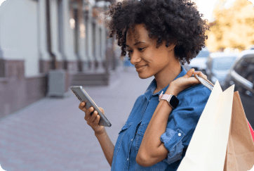 An image of a lady smiling at her phone with her purchase slung across her shoulder.
